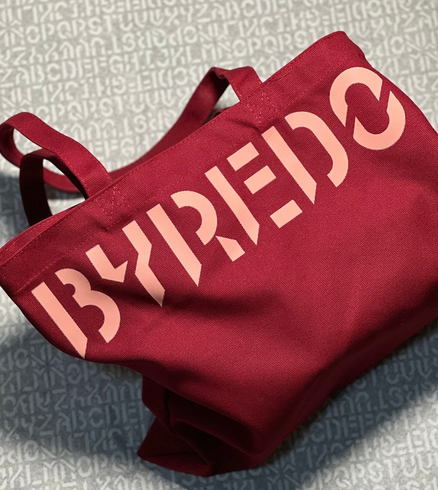 Burgundy BYREDO canvas tote bag with light pink BYREDO logo printed across the front.