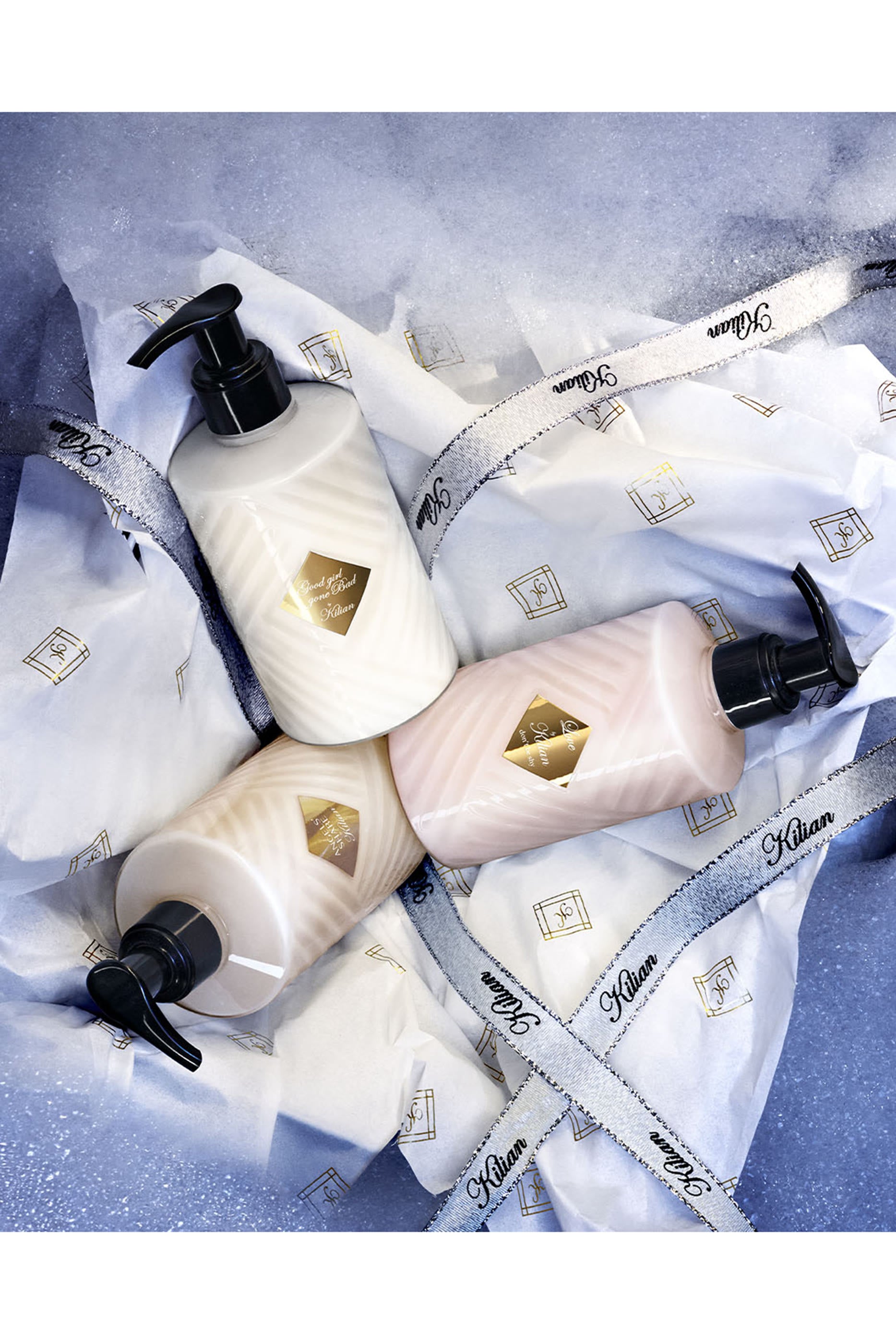 Three Kilian Angels’ Share body lotion pump bottles arranged on branded tissue paper with Kilian ribbon
