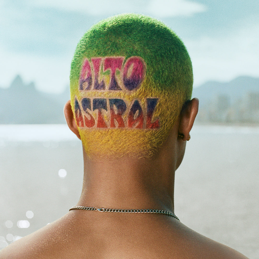 Person with colorful shaved head with 'ALTO ASTRAL' text, standing by a body of water.