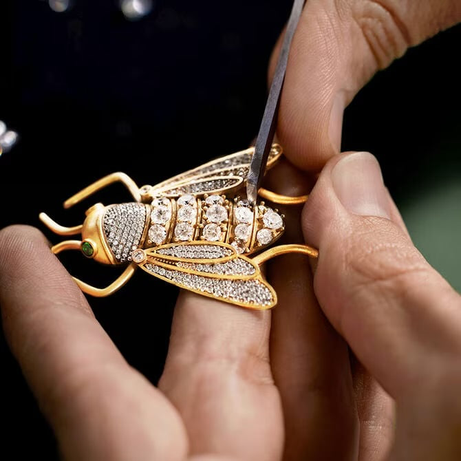 Gold insect-shaped jewelry with gemstones being adjusted by a person.