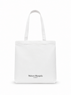 A white canvas tote bag with long handles and the black printed text 'Maison Margiela PARIS' near the bottom center, shown on a clean white background.