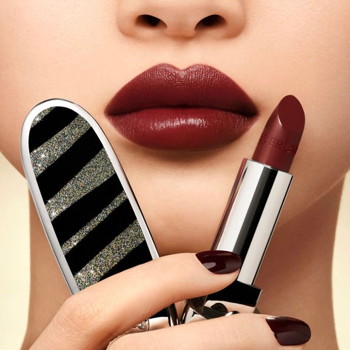 Close-up of a person holding a Guerlain lipstick with a mirror case, showing a close-up of lips.