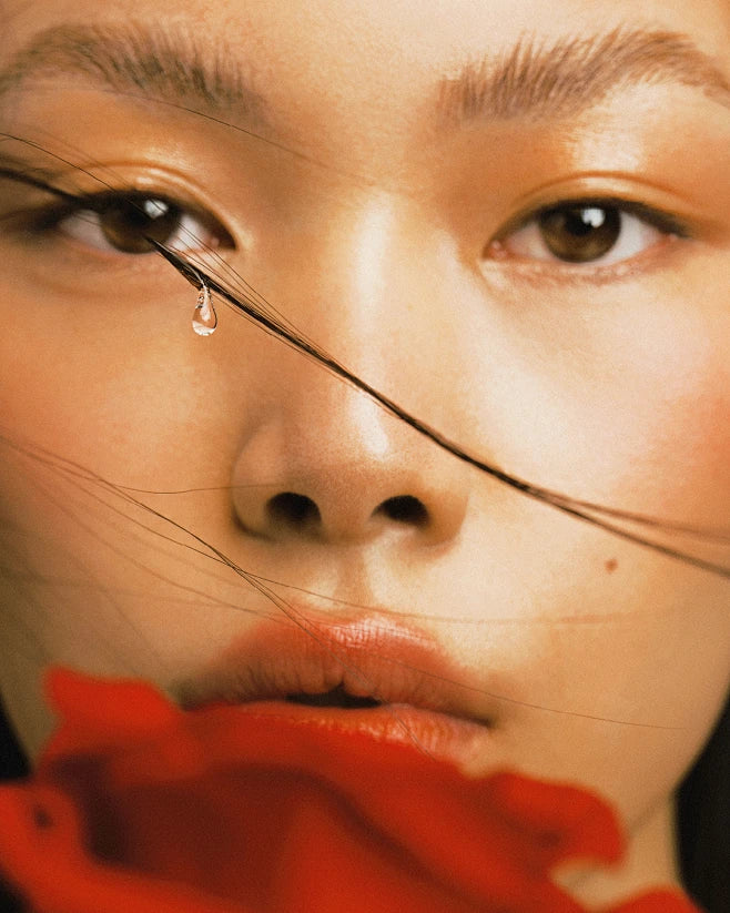 Close-up of a person's face with a red flower, artistic and emotional. byredo ad