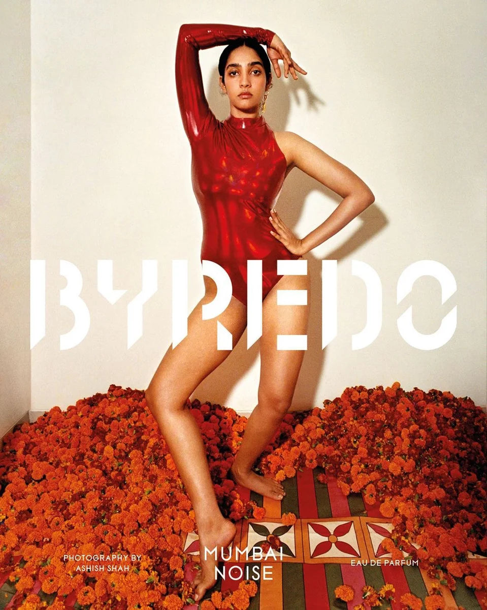 Person in a red outfit surrounded by flowers with Byredo branding