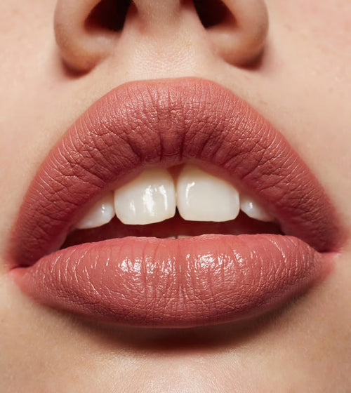 Close-up of lips wearing BYREDO Earth Dust lipstick in a warm nude-brown satin finish, showing smooth texture and natural makeup look.