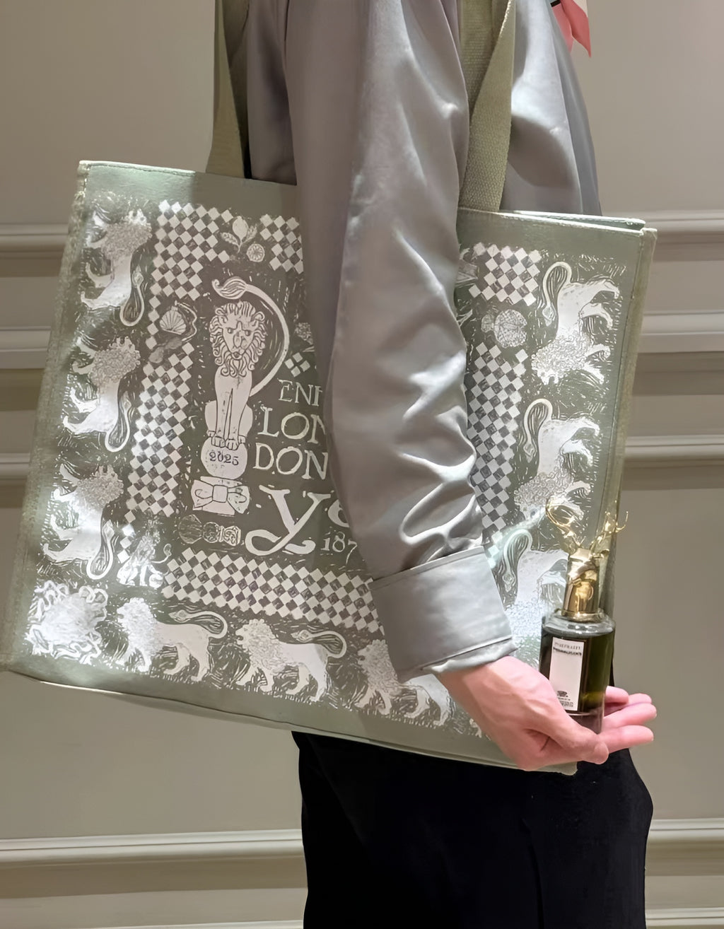 Person holding a decorative tote bag with intricate patterns and a bottle of perfume.