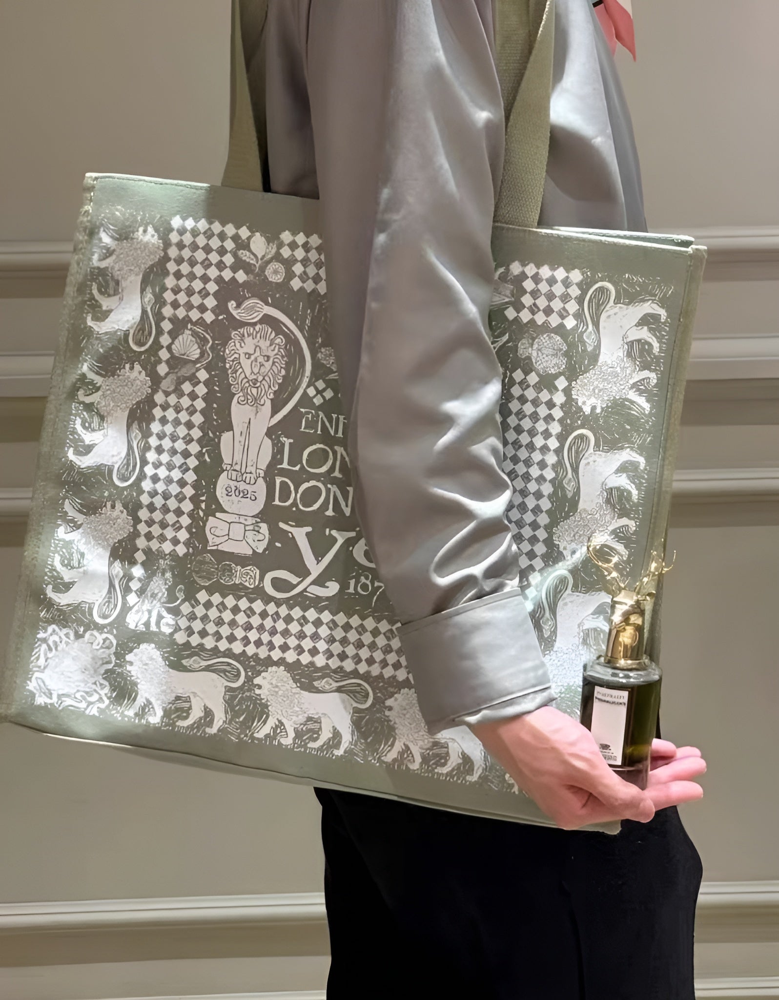 Person holding a decorative tote bag with intricate patterns and a bottle of perfume.