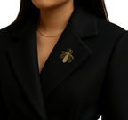 Person wearing a black blazer with a gold brooch on a white background