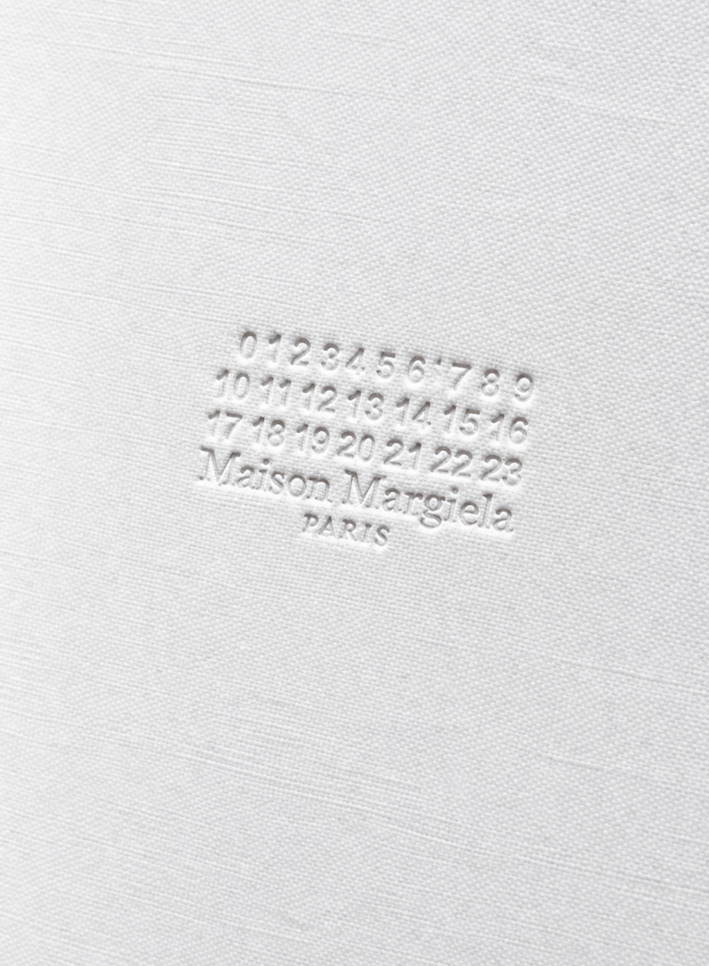 Close-up of embossed Maison Margiela Paris logo and signature number motif on textured white notebook cover at Exquisite.