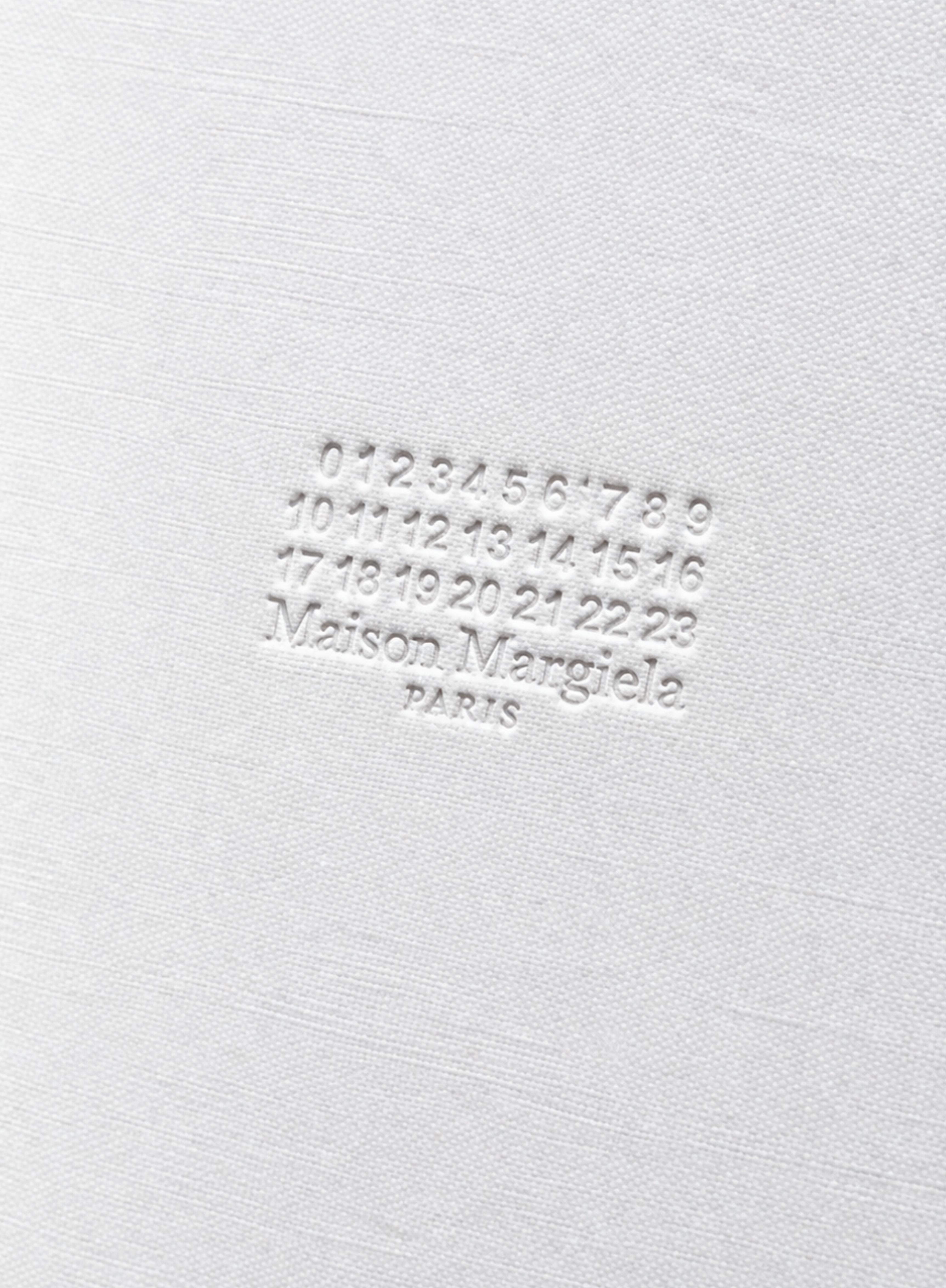 Close-up of embossed Maison Margiela Paris logo and signature number motif on textured white notebook cover at Exquisite.