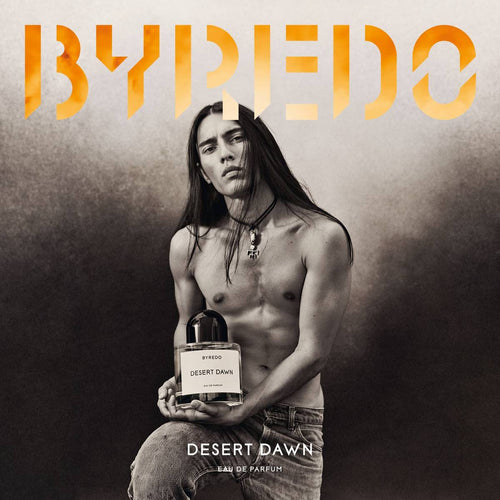 Man holding a Byredo Desert Dawn perfume bottle against a dark background