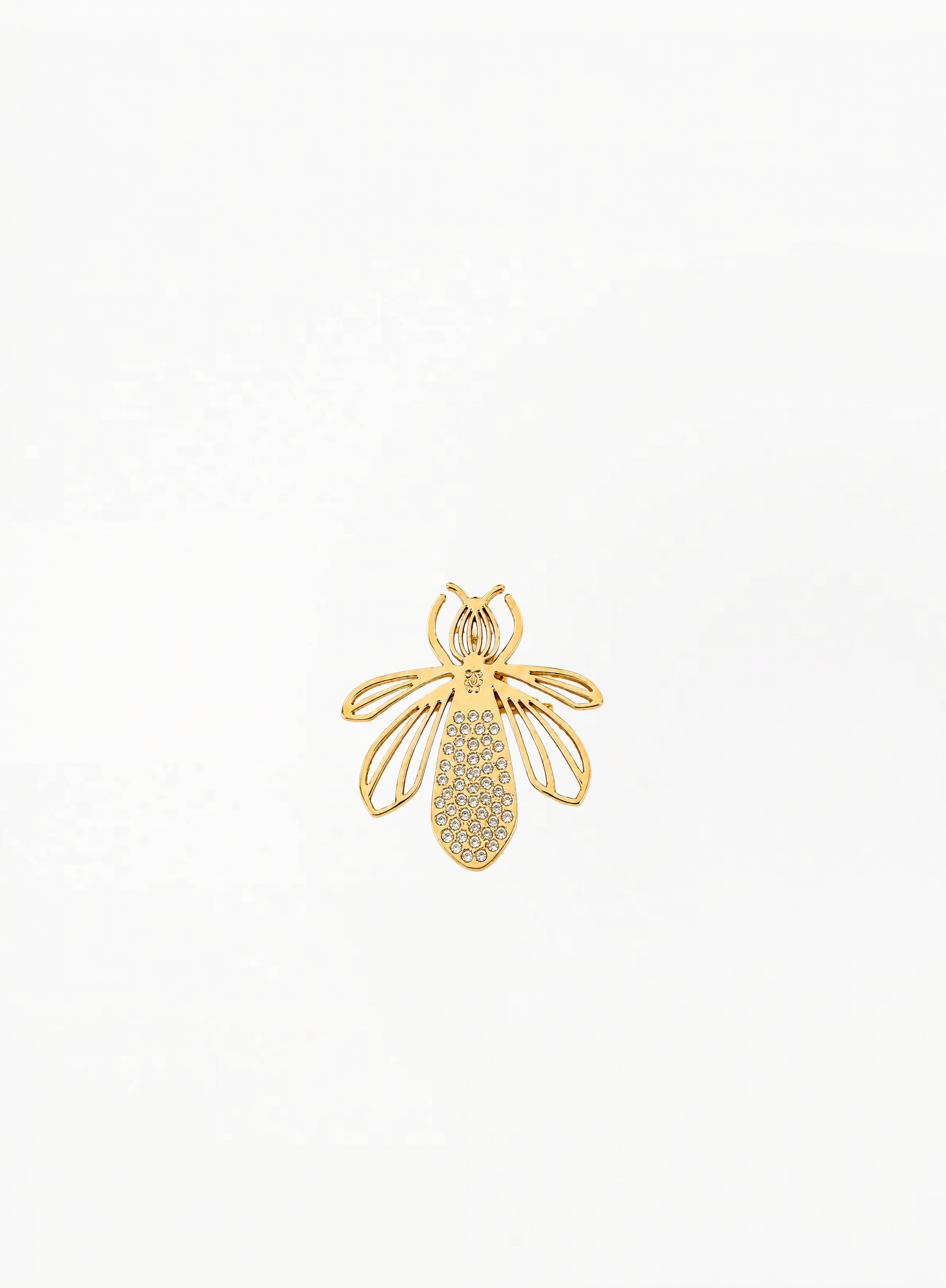 Guerlain gold bee charm, brooch with openwork wing details, displayed on a clean elegant background featuring refined luxury accessory craftsmanship and minimalist decorative design.