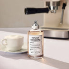 Bottle of Maison Margiela replica perfume with a cup of coffee and espresso machine in the background