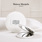 Maison Margiela Paris limited edition compact mirror with a white canvas pouch featuring the iconic numeric label, displayed open on a white surface with a minimalist luxury background.