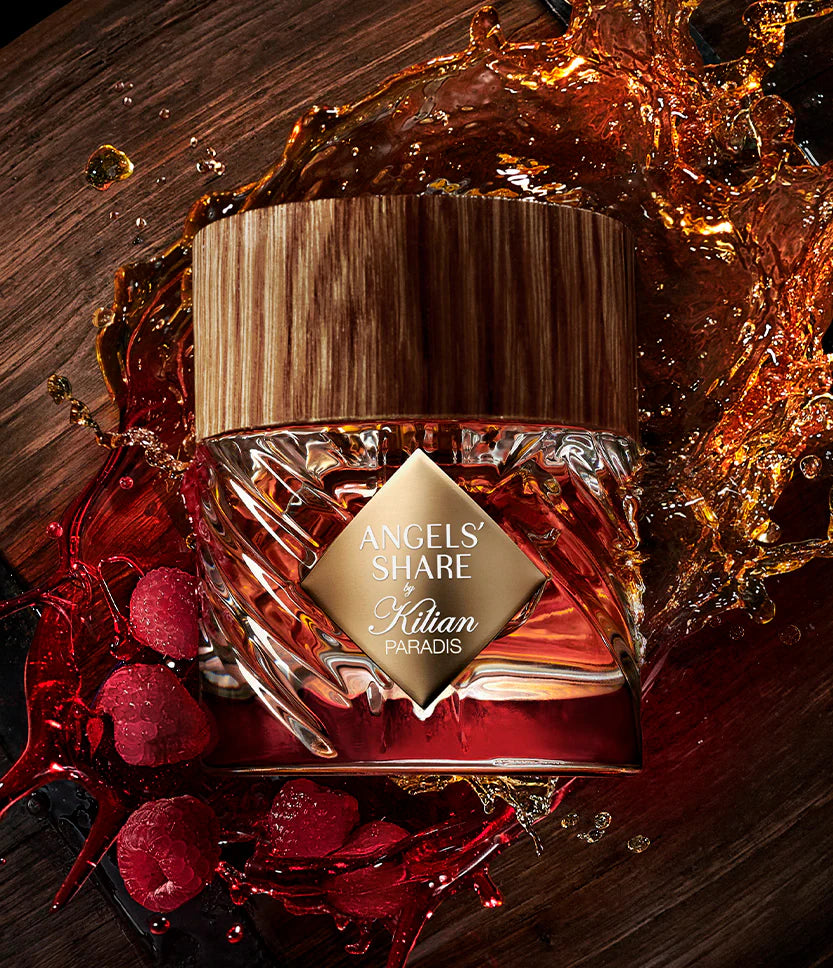 Kilian Angels' Share Paradis perfume bottle with red berries and liquid splashes on a dark background