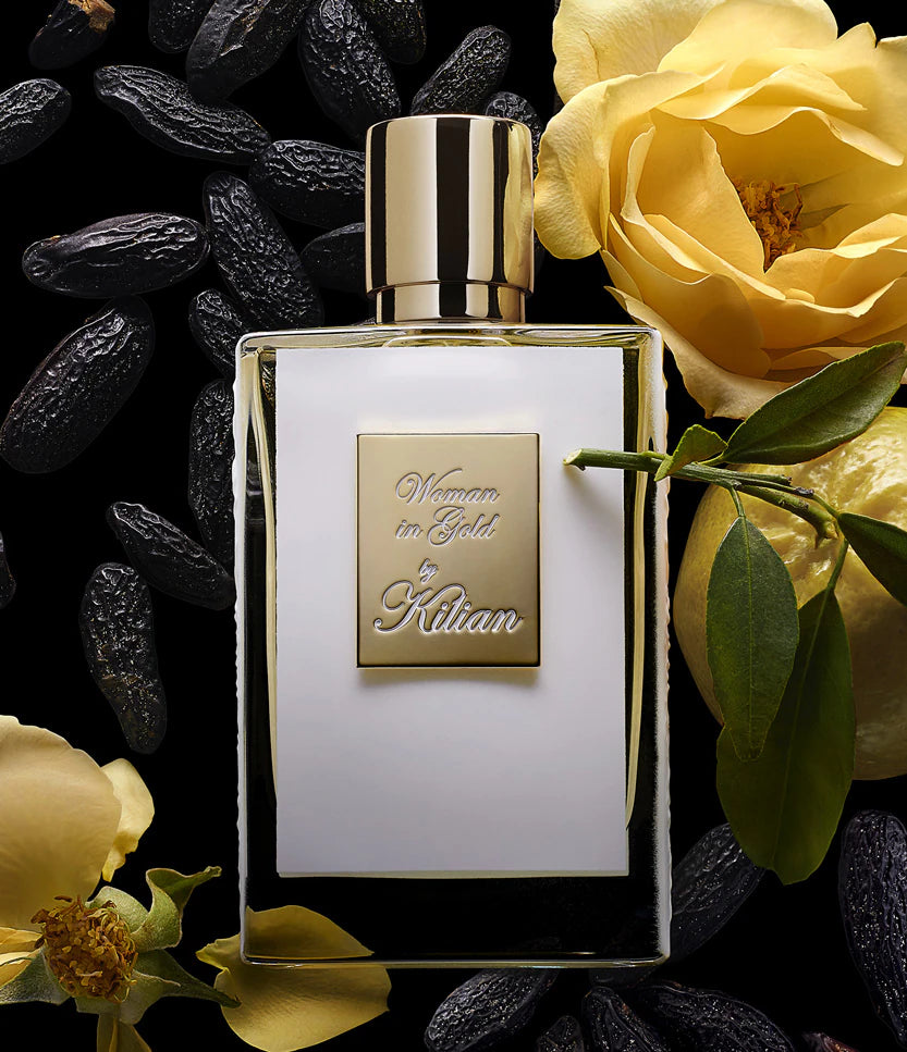 Perfume bottle labeled 'Woman in Gold' by Kilian with yellow flowers and dark berries on a black background