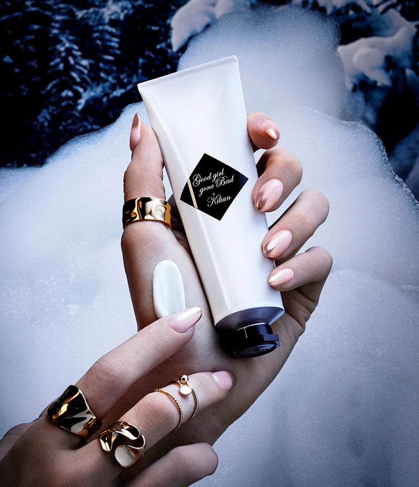 Hand holding Kilian Good Girl Gone Bad hand cream 50ml with blurred snowy background, luxury skincare visual
